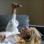 Woman lounging on sofa taking a selfie at home during the day.