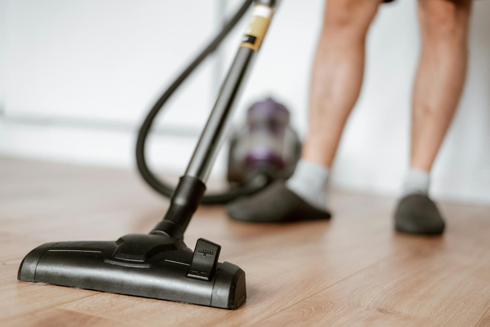 A person uses a vacuum cleaner on a wooden floor for effective cleaning.