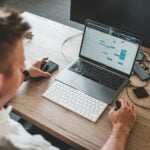 man holding mouse and iPhone while using Macbook Pro