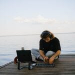 a man sitting on a dock working on a laptop