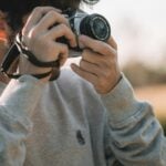woman in gray sweater holding black dslr camera