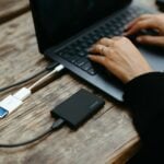 Hands typing on laptop connected to external hard drive.