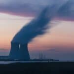 skyline photography of nuclear plant cooling tower blowing smokes under white and orange sky at daytime