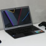 black and gray laptop computer near black wireless game controller on wooden table