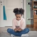 girl in white sweater and blue denim jeans sitting on floor
